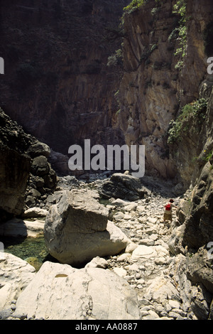 Femme solitaire négociant les rochers ensoleillés parsemés de rochers presque asséché sur le lit de la rivière dans la gorge de Samaria, Crète entourée de falaises verticales Banque D'Images