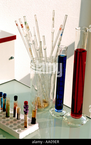 Diverses pipettes transparentes sont présentées dans un bocal à côté de verrerie contenant des liquides rouges et bleus. Banque D'Images