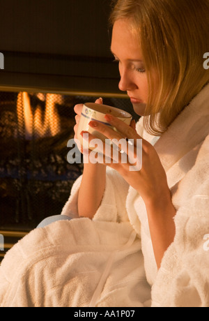 Jeune femme en peignoir gorgées boisson chaude par cheminée USA Banque D'Images