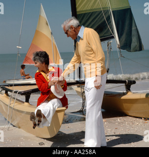 Vieux couple clown dans un mode amusant dans un paramètre de plage tout en restant assis sur un catamaran voilier sur le sable Banque D'Images