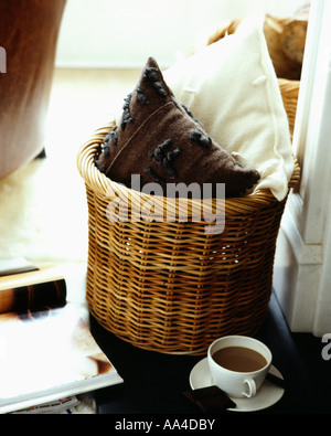 Close-up de crème et marron coussins molletonnés dans panier en osier avec une tasse de café à l'étage Banque D'Images