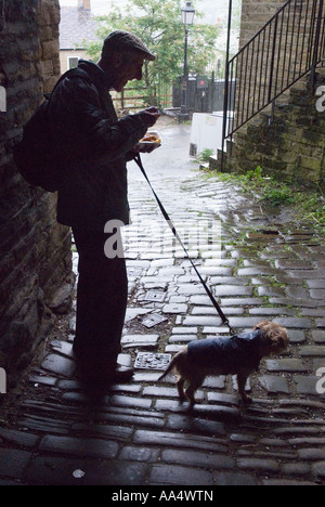 Un vieil homme et son chien à l'abri de la pluie dans une ruelle l'homme est de manger une portion de frites Banque D'Images