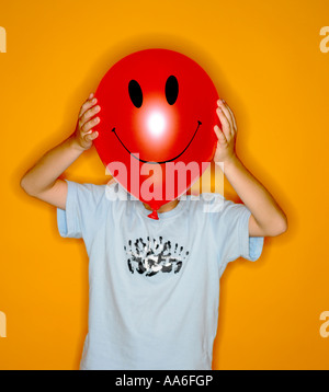 Enfant tenant un ballon en face de son visage avec un grand sourire heureux sur elle Banque D'Images