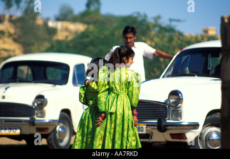 Deux jeunes filles indiennes en vert entre deux voitures ambassadrice blanches, Jaisalmer, Rajasthan, Inde du Nord Banque D'Images