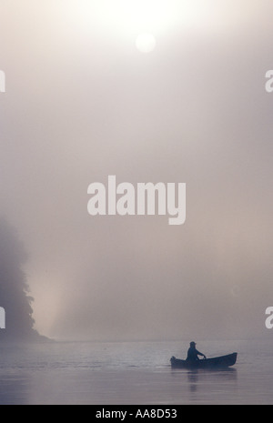 Un canot glisse à travers le brouillard et la brume d'un matin d'été sur la rivière Restigouche, dans le nord du Nouveau-Brunswick, Canada Banque D'Images