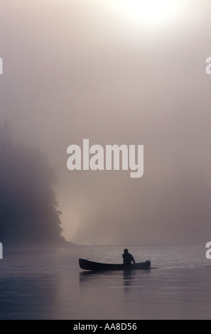 Un canot glisse à travers le brouillard et la brume d'un matin d'été sur la rivière Restigouche, dans le nord du Nouveau-Brunswick, Canada Banque D'Images