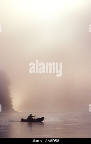 Un canot glisse à travers le brouillard et la brume d'un matin d'été sur la rivière Restigouche, dans le nord du Nouveau-Brunswick, Canada Banque D'Images