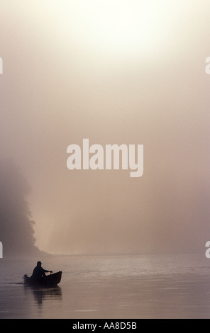 Un canot glisse à travers le brouillard et la brume d'un matin d'été sur la rivière Restigouche, dans le nord du Nouveau-Brunswick, Canada Banque D'Images