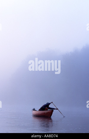 Un canot glisse à travers le brouillard et la brume d'un matin d'été sur la rivière Restigouche, dans le nord du Nouveau-Brunswick, Canada Banque D'Images