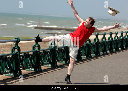 Un excès de middle-aged man doing maladroit kicking élevé danse de routine sur le front de mer de Brighton que son chapeau s'ouvre dans la brise Banque D'Images