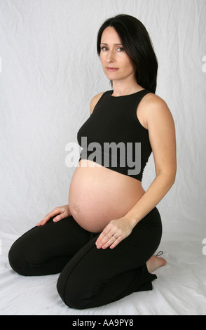 Femme enceinte agenouillée portant un gilet et un pantalon noir