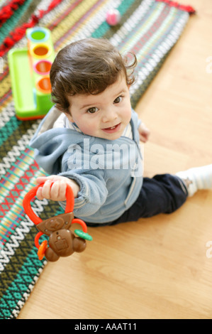 Baby Boy sitting dans le plancher holding a toy et regardant la caméra Banque D'Images