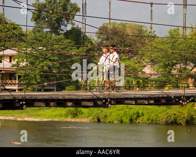 Des écoliers d'ajo sur les bicyclettes de traverser un pont sur le chemin de la maison Vang Vieng Laos Banque D'Images