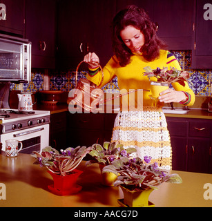 Jeune femme au foyer dans sa cuisine son arrosage Les Violettes africaines sur la table de cuisine Banque D'Images