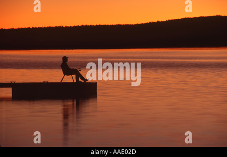 Un pêcheur de poissons du lac un dock comme il aime le soleil ou de coucher de soleil Banque D'Images