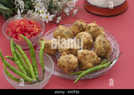 en-cas indien boulettes de pommes de terre frites neuf batata ama avec épicé vert froid et tomates dans une assiette en verre sur fond rose Banque D'Images