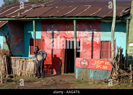 Homme debout à l'extérieur de l'atelier avec Coca Cola signes dans village de Dejen près de Shafartak Afrique Ethiopie pont Banque D'Images