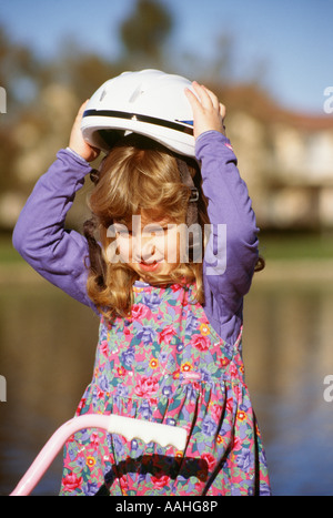 Jeune fille 4 - 6 ans maintenant de mettre un casque de vélo sur la tête assis sur l'activité vélo US USA United States. M. © Myrleen Pearson .....Ferguson Cate Banque D'Images