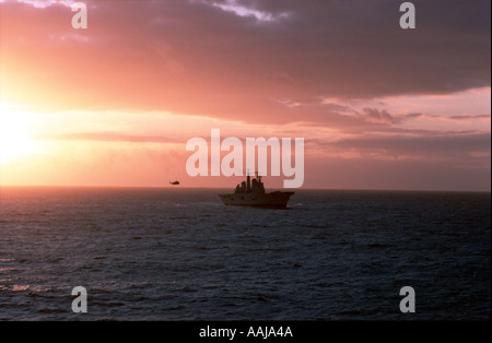 Porte-avions en mer avec l'hélicoptère dans le coucher du soleil Banque D'Images
