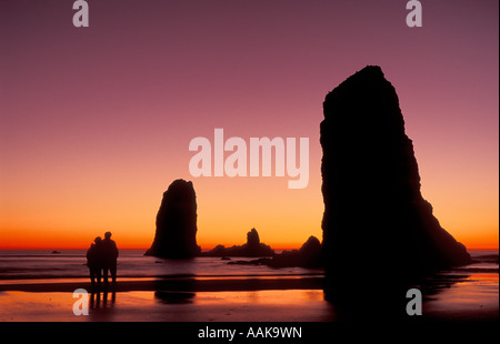 Haystack Rock piles de la mer au coucher du soleil avec couple on beach Cannon Beach Oregon coast Banque D'Images