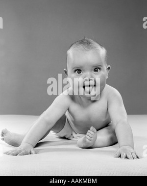 1950 PORTRAIT DE BABY SITTING ET STICKING TONGUE OUT LOOKING AT CAMERA Banque D'Images