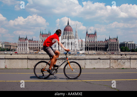Un homme fait du vélo le long du Danube avec vue sur le bâtiment du Parlement hongrois en arrière-plan à Budapest Hongrie Banque D'Images
