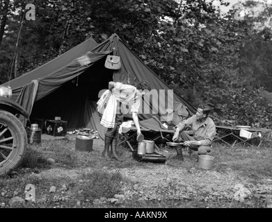 1920 HOMME FEMME COUPLE SUR LA PÊCHE VOYAGE DE CAMPING LOCATIONS DE CAMPING MAN LA CUISSON À FEU Banque D'Images