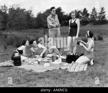 Années 30, groupe de cinq jeunes hommes & femmes bénéficiant de pique-niquer dans les bois TOUS, SAUF UN, portant des maillots de bain Banque D'Images