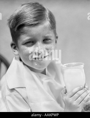 1930 ROUSSEUR SMILING FACE BOY LOOKING AT CAMERA AVEC UNE MOUSTACHE DE LAIT ET LA GOUTTE DE LAIT SUR LE MENTON DE VERRE DE LAIT Banque D'Images