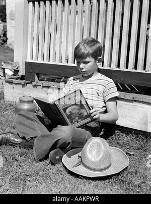 1940 garçon en jeans et T-shirt à rayures PORCHE APPUYÉ CONTRE LA LECTURE DU LIVRE Vingt mille lieues sous la mer Banque D'Images