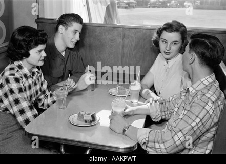 Années 50, deux adolescents DES COUPLES AU STAND IN DINER portant des chemises à carreaux de couleur SOLIDE ET SODAS POTABLE PARLER ENSEMBLE Banque D'Images