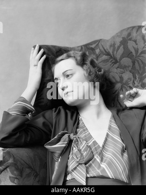 1930 Femme assise dans une chaise à dossier haut de réfléchi ou expression du visage mélancolique Banque D'Images