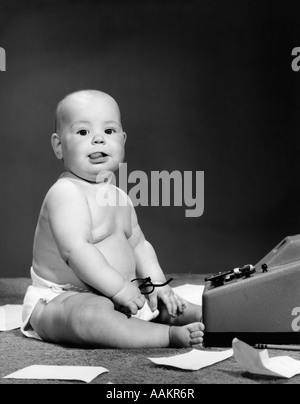 Années 1950 Années 1960 BÉBÉ EN COUCHE STICKING OUT TONGUE HOLDING GLASSES SÉANCE AVANT L'AJOUT DE MACHINE LOOKING AT CAMERA Banque D'Images