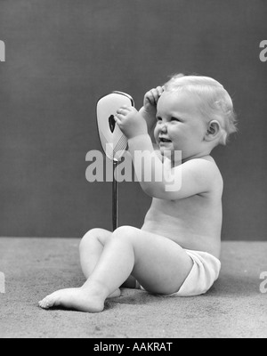 1940 BLOND BÉBÉ GIRL HOLDING MIROIR DE REGARDER SES CHEVEUX Banque D'Images