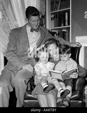 1940 FEMME MÈRE EN FAUTEUIL DE LECTURE Fille Garçon Fille Fils avec fier homme père regardant Banque D'Images