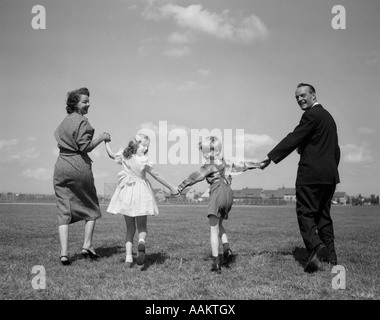 1950 SMILING HAPPY FAMILY Mère Père BOY GIRL HOLDING HANDS WALKING AWAY SUR L'herbe se retourna LOOKING AT CAMERA Banque D'Images