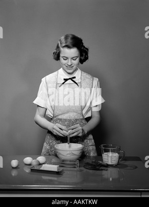 1950 JEUNES TEENAGE GIRL WEARING APRON ROUES oeuf dans un récipient de cuisson Cuisson Banque D'Images