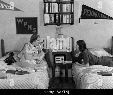 Années 1930 Années 1940 DEUX ADOLESCENTES couché sur des lits de dortoir prix adapté à l'ÉCOUTE DE LA RADIO COLLEGE SCHOOL FANIONS SUR MUR Banque D'Images