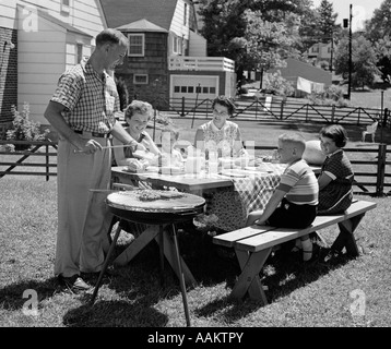 Années 1950 DANS LA COUR DE LA FAMILLE LA CUISSON des hot dogs SITTING AT TABLE DE PIQUE-NIQUE Banque D'Images