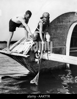 Années 1920 L'HOMME ET LA FEMME en costume de bain en crabe au large de vieux bateaux en bois abandonnés Banque D'Images