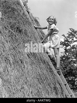 1940 SMILING BLONDE GIRL CLIMBING LADDER APPUYÉ CONTRE GRAND FOIN PILE Banque D'Images