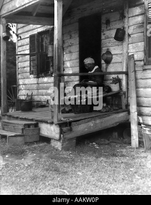 Années 1920 Années 1930 PERSONNES ÂGÉES AFRICAN AMERICAN WOMAN SITTING ON PORCH DE PETITE MAISON EN BOIS Banque D'Images