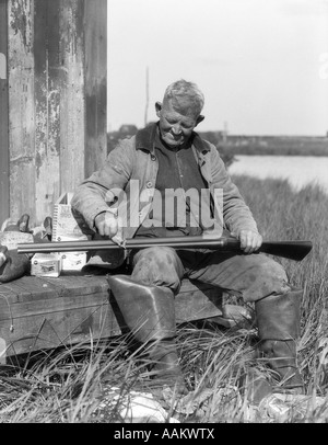 Années 1920 Années 1930 SENIOR MAN SITTING ON BENCH Fusil de chasse aux canards NETTOYAGE BARNEGAT BAY, NEW JERSEY, USA Banque D'Images