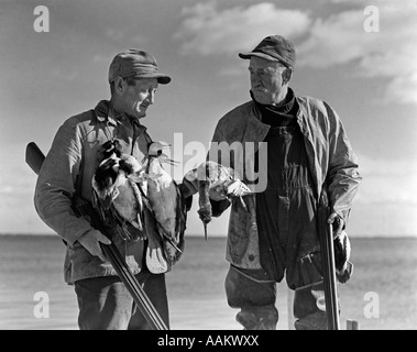 Années 1930 Années 1940 DEUX HOMMES TENANT DES FUSILS DE CHASSE AU CANARD CANARDS MORTS HOLDING BARNEGAT BAY, NEW JERSEY, USA Banque D'Images