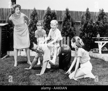 1960 FAMILLE DE CINQ Arrière-cour EN DONNANT DES TOURS À PAPA de ferroutage ENFANTS Banque D'Images