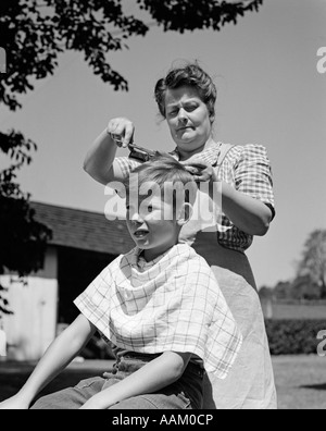 1940 FARMWIFE MÈRE GARÇON COUPE LES CHEVEUX DE SON FILS À L'EXTÉRIEUR SOUS UN ARBRE Banque D'Images