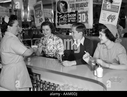 1950 SMILING WAITRESS FEMME DEUX ADOLESCENTES ET UN GARÇON À DINER COUNTER Banque D'Images