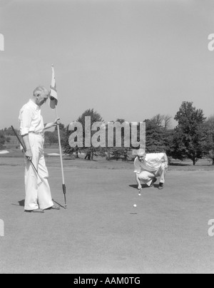 1930 1940 Hommes âgés SUR UN DRAPEAU VERT GOLF HOLDING L'autre s'agenouille en alignant son putt Banque D'Images