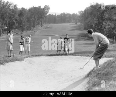 Années 1920 Années 1930 L'HOMME DANS LES CULOTTES DE GOLF À FOSSE DE SABLE AVEC DES HOMMES ET FEMMES À LA RECHERCHE SUR Banque D'Images