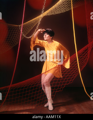 1970 JEUNE FEMME EN Robe tunique d'or court ENTRE LES CORDES ET FILETS DE DANSE Banque D'Images